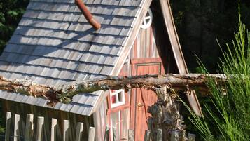 A rustic wooden building with a sloped roof, a wooden fence, and a tree branch in the foreground.