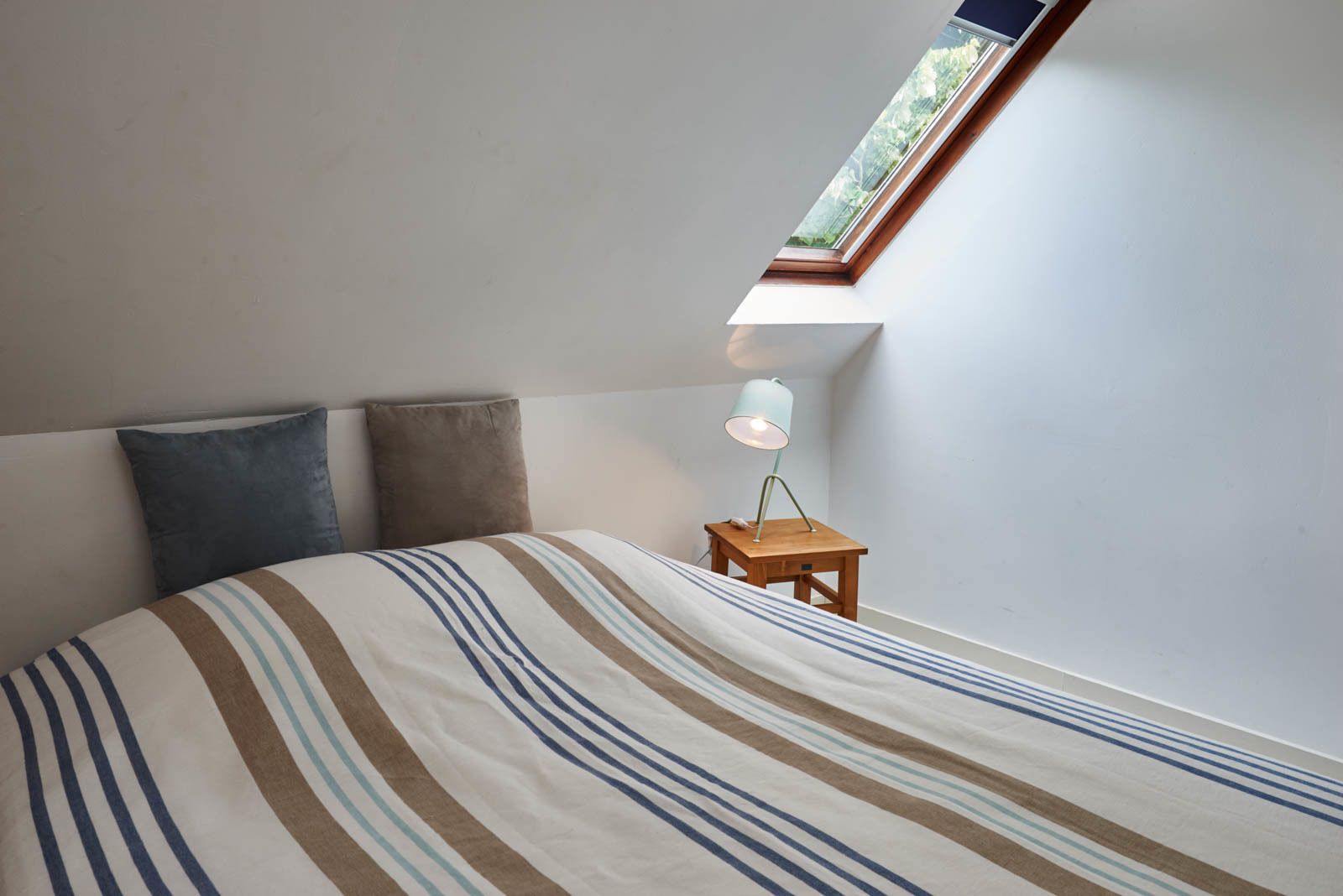 A bedroom with a bed, two pillows, a nightstand with a lamp, and a skylight.