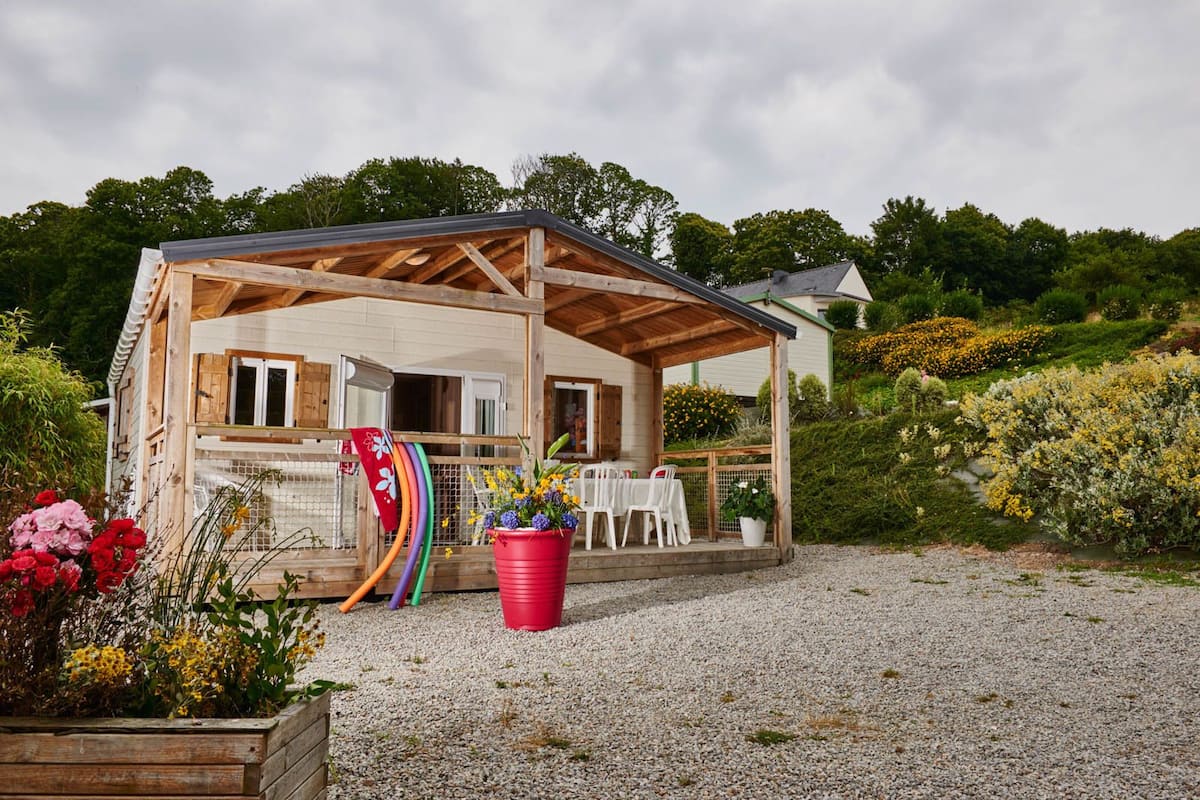Een houten gebouw met een overdekte veranda, een omheind terras met stoelen en een grindpad.