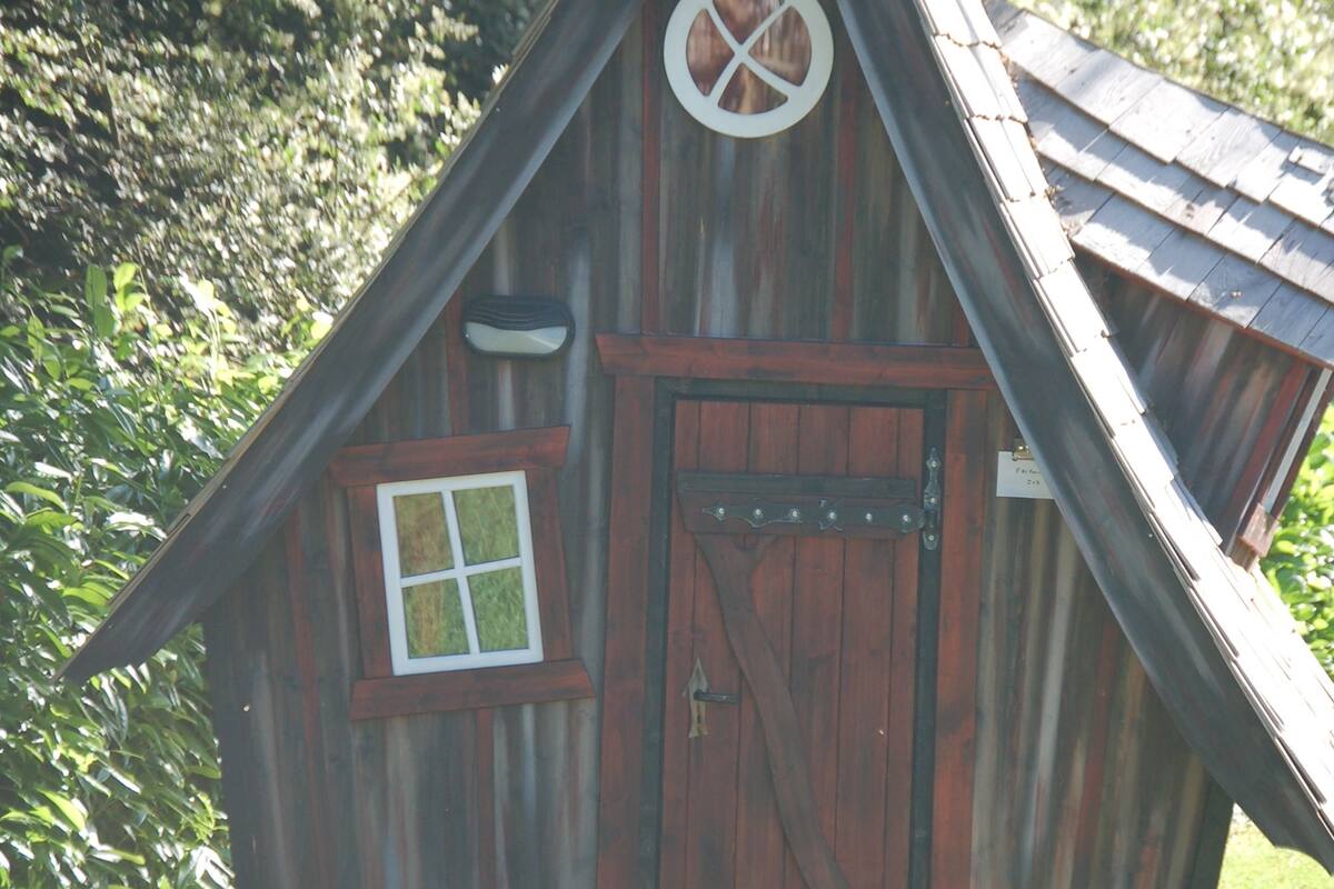 Een rustieke houten hut met een puntig dak, een houten deur en een klein raam.