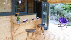 Een houten terras met een bar, twee barkrukken en een paarse stoel.