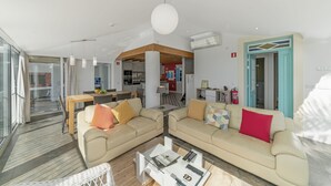 Una sala de estar moderna con dos sofás beige, una mesa de centro de vidrio y un comedor al fondo.