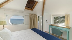 Un dormitorio con una cama grande, un escritorio y vista al mar a través de una ventana.