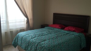 Une chambre à coucher avec un lit, une table de chevet, une fenêtre avec des rideaux et une tête de lit.