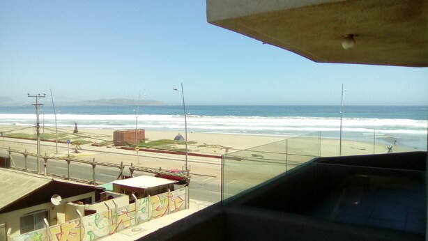 Une vue sur une plage depuis un balcon, avec un ciel dégagé, une plage de sable et l’océan.