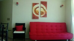 Un salon avec un canapé rouge, un fauteuil noir doté d’un coussin rouge et deux tableaux abstraits accrochés au mur.