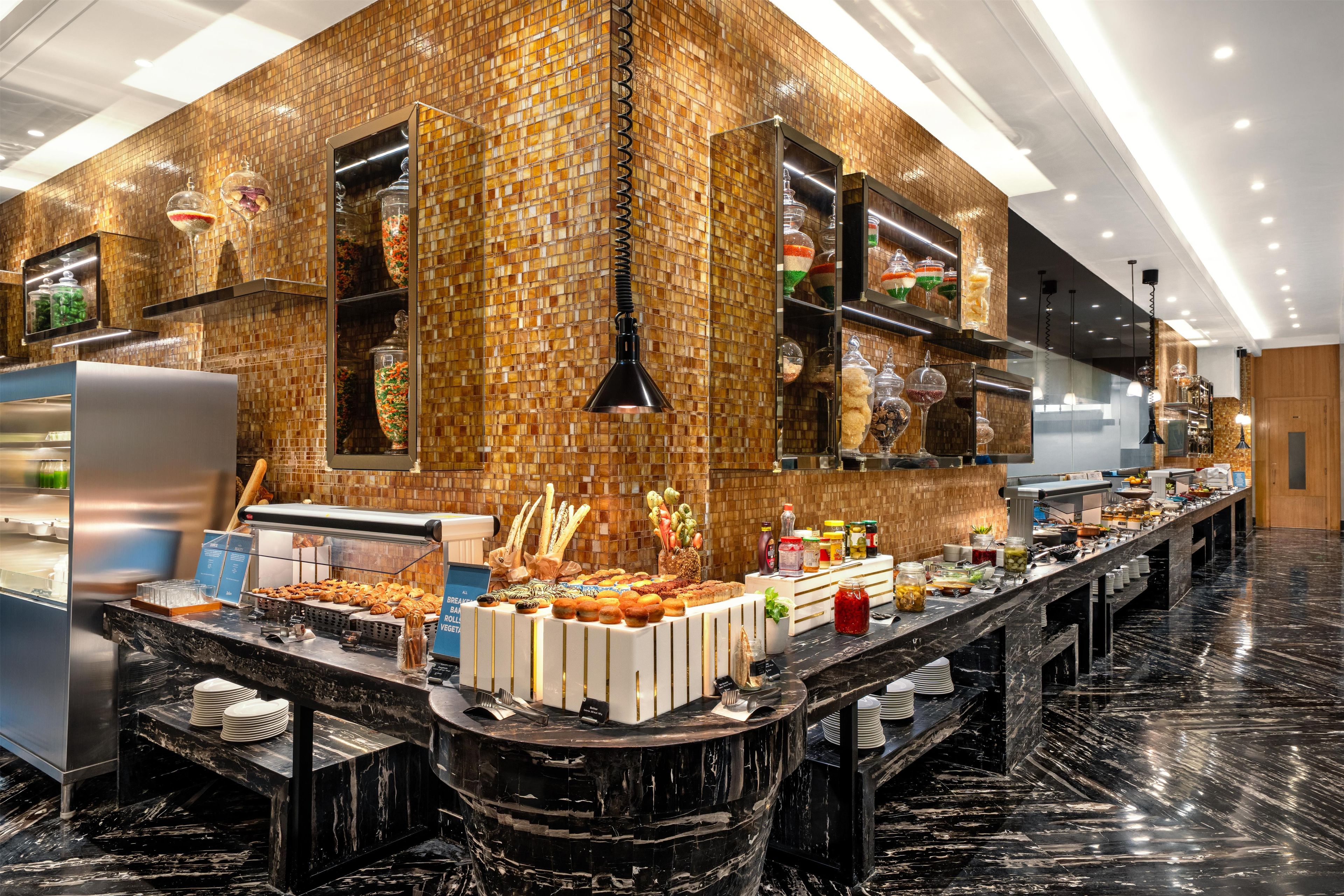 A modern hotel kitchen with a marble countertop, buffet setup, and a mosaic tile wall.