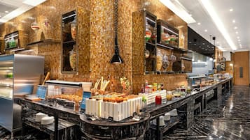 A modern hotel kitchen with a marble countertop, buffet setup, and a mosaic tile wall.