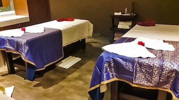 Two single beds with white bedding and blue blankets sit against a wall with a window above, offering a view.