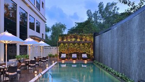 A swimming pool with lounge chairs and umbrellas, surrounded by a wooden pergola and a wall with greenery. - Radisson Mumbai Andheri MIDC (Mumbai)