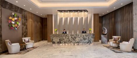 A spacious lobby with a marble reception desk, modern chairs, and a decorative wall with colorful glass pieces.
