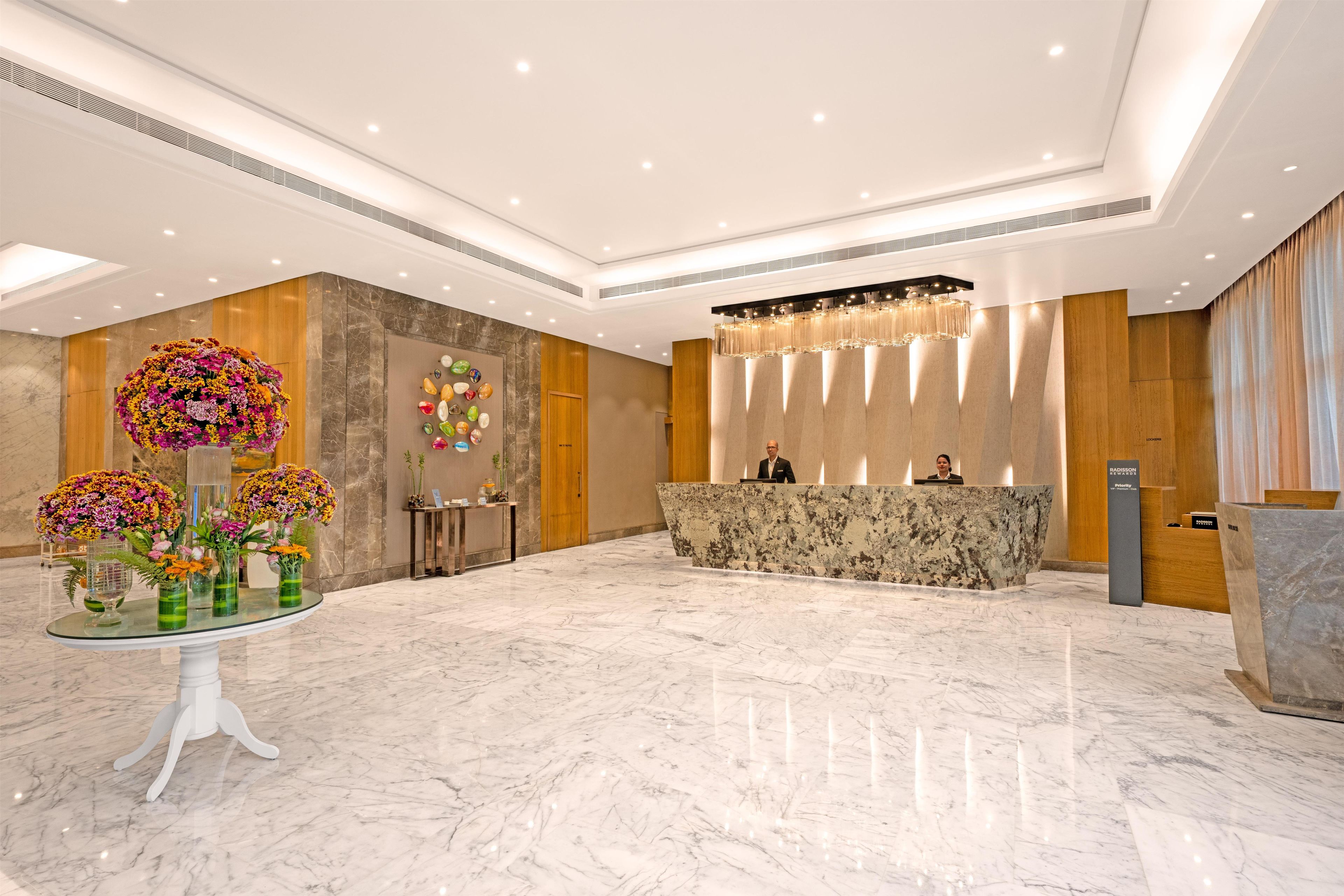 A hotel reception area with a marble floor, a reception desk, and a large floral arrangement.