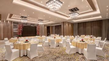Un salón de banquetes con mesas redondas, sillas blancas, candelabros y una alfombra estampada.