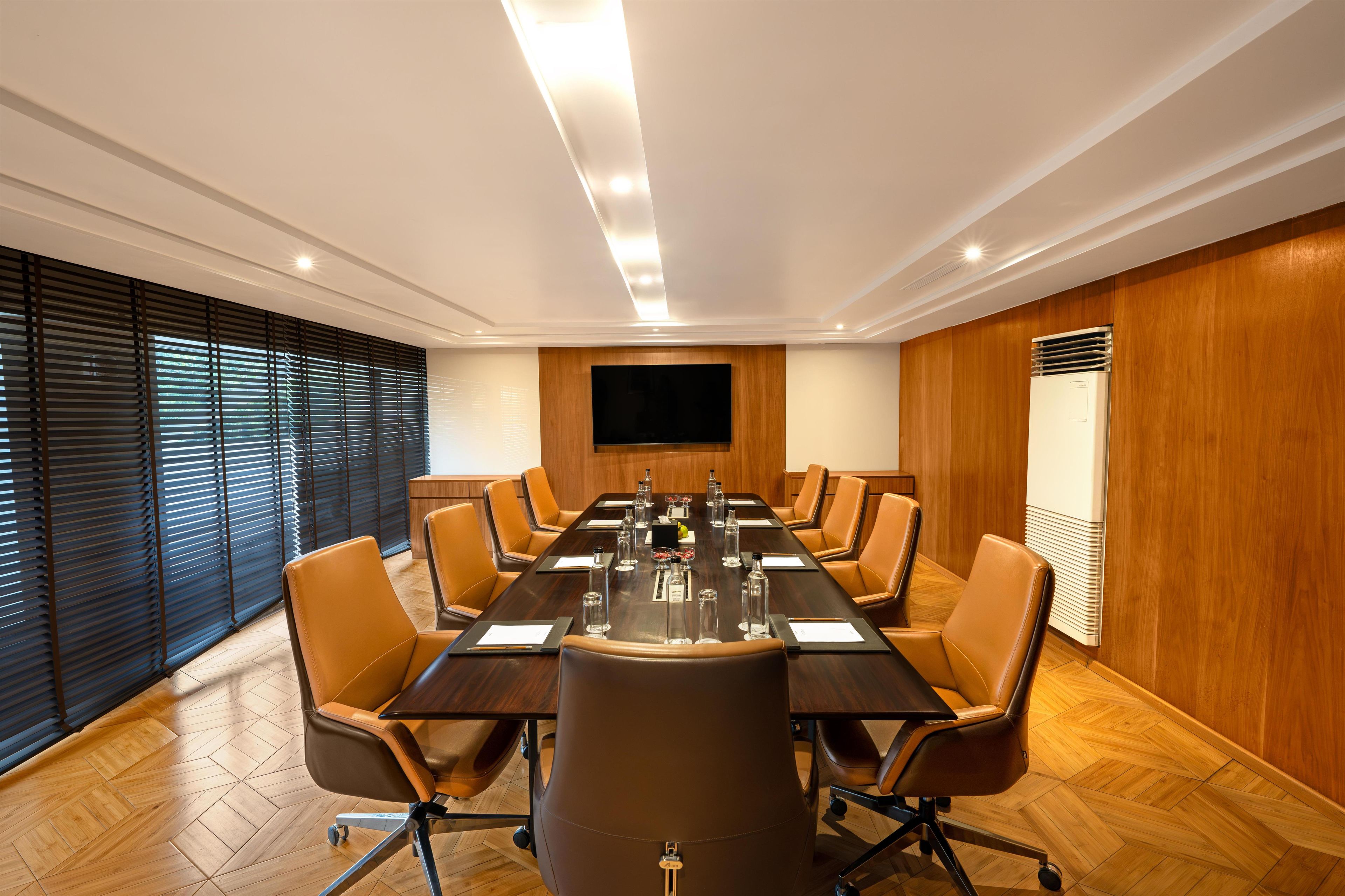 A conference room with a long table, chairs, a flat-screen TV, and wooden paneling.