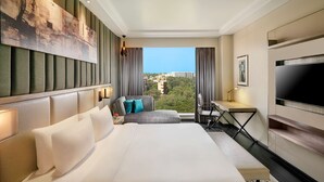 A hotel room with a large bed, a desk, a chair, a TV, and a view of the city. - Radisson Mumbai Andheri MIDC (Mumbai)