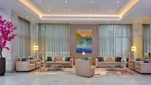 A spacious lobby with a marble floor, two sofas with colorful cushions, a large painting on the wall, and large windows with sheer curtains. - Radisson Mumbai Andheri MIDC (Mumbai)