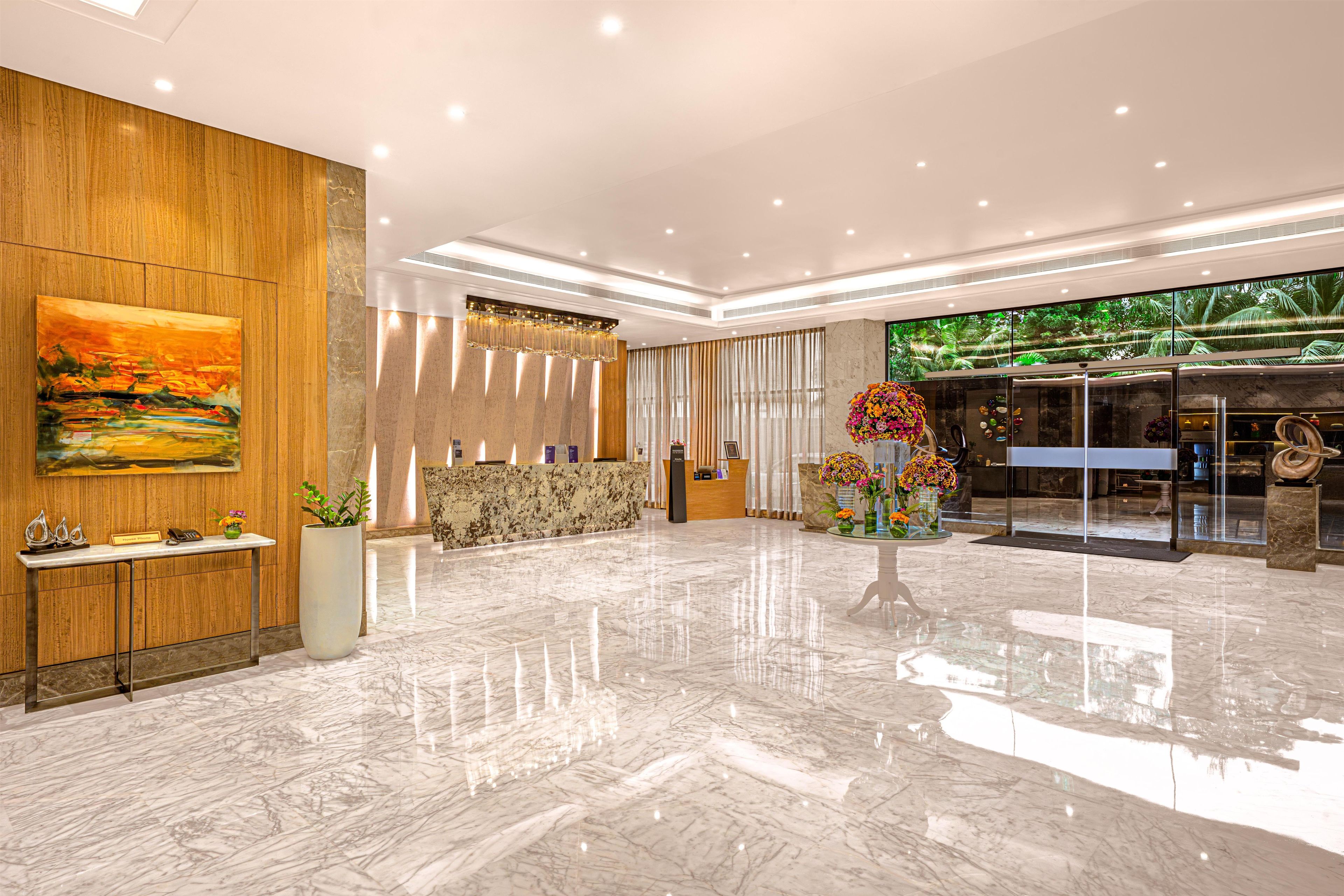 A modern lobby with a reception desk, a large painting, and a glass wall with a tropical view.