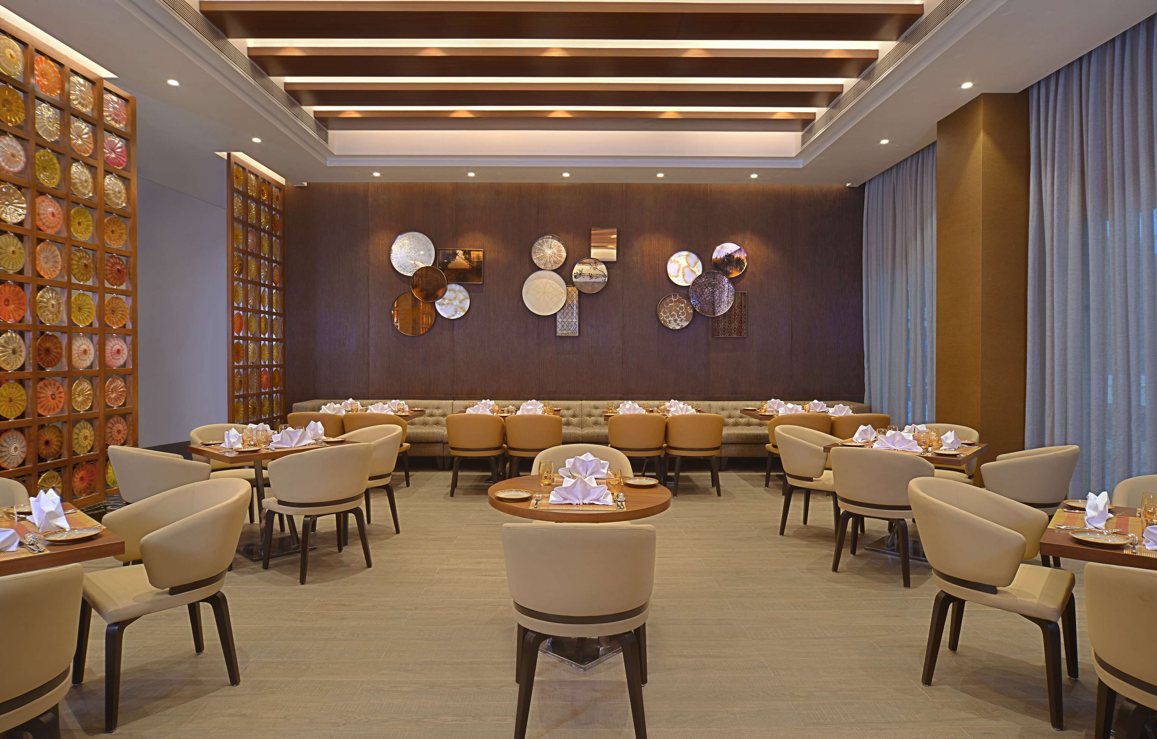 Un espace de restauration d’hôtel avec des tables rondes, des sièges confortables et des œuvres d’art décoratives sur les murs.