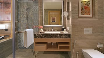 Un baño moderno con ducha envuelta en vidrio, lavamanos de mármol y un espejo grande arriba.