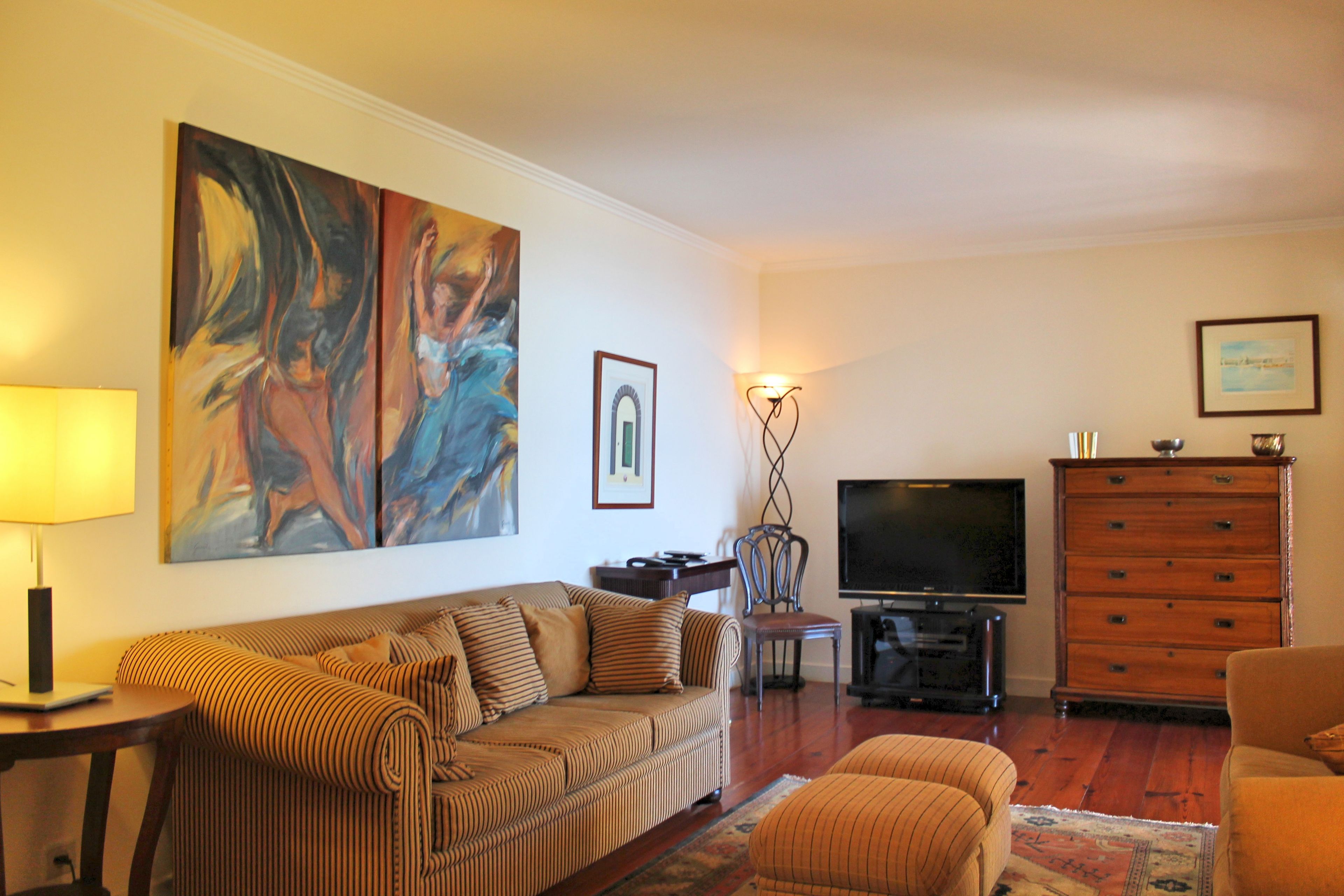 A living room with a sofa, a television, a wooden cabinet, and a painting on the wall.