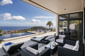 Un'area relax esterna moderna con piscina, lettini e vista sul mare e sulla città.