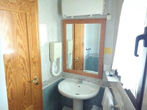 Une salle de bain avec une porte en bois, un lavabo blanc, un miroir avec un cadre en bois et un espace douche.