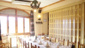 Ein Essbereich mit einem langen Tisch, der für eine Mahlzeit gedeckt ist, Holzsesseln, einer Kristallleuchter und einem großen Fenster mit Vorhängen.