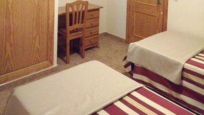 Ein Zimmer mit einem Holzkleiderschrank, einem Schreibtisch mit Stuhl, einem an der Wand montierten Fernseher und zwei Betten mit gestreifter Bettwäsche.
