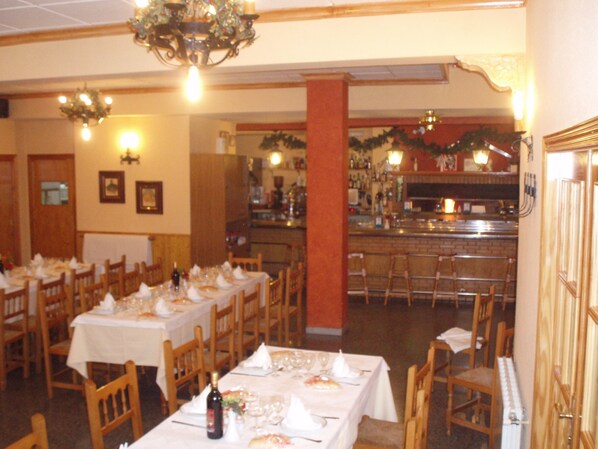 A restaurant with multiple tables set for dining, a bar area, and a kitchen in the background. - Hotel Meson El Castillo (Banyeres de Mariola)