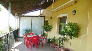 Eine überdachte Terrasse mit Tisch, Stühlen, Topfpflanzen und einem Geländer.
