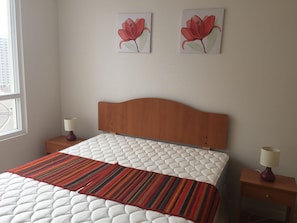 Une chambre à coucher comprenant un lit, deux tables de chevet, une fenêtre et deux tableaux représentant des fleurs, accrochés au mur.