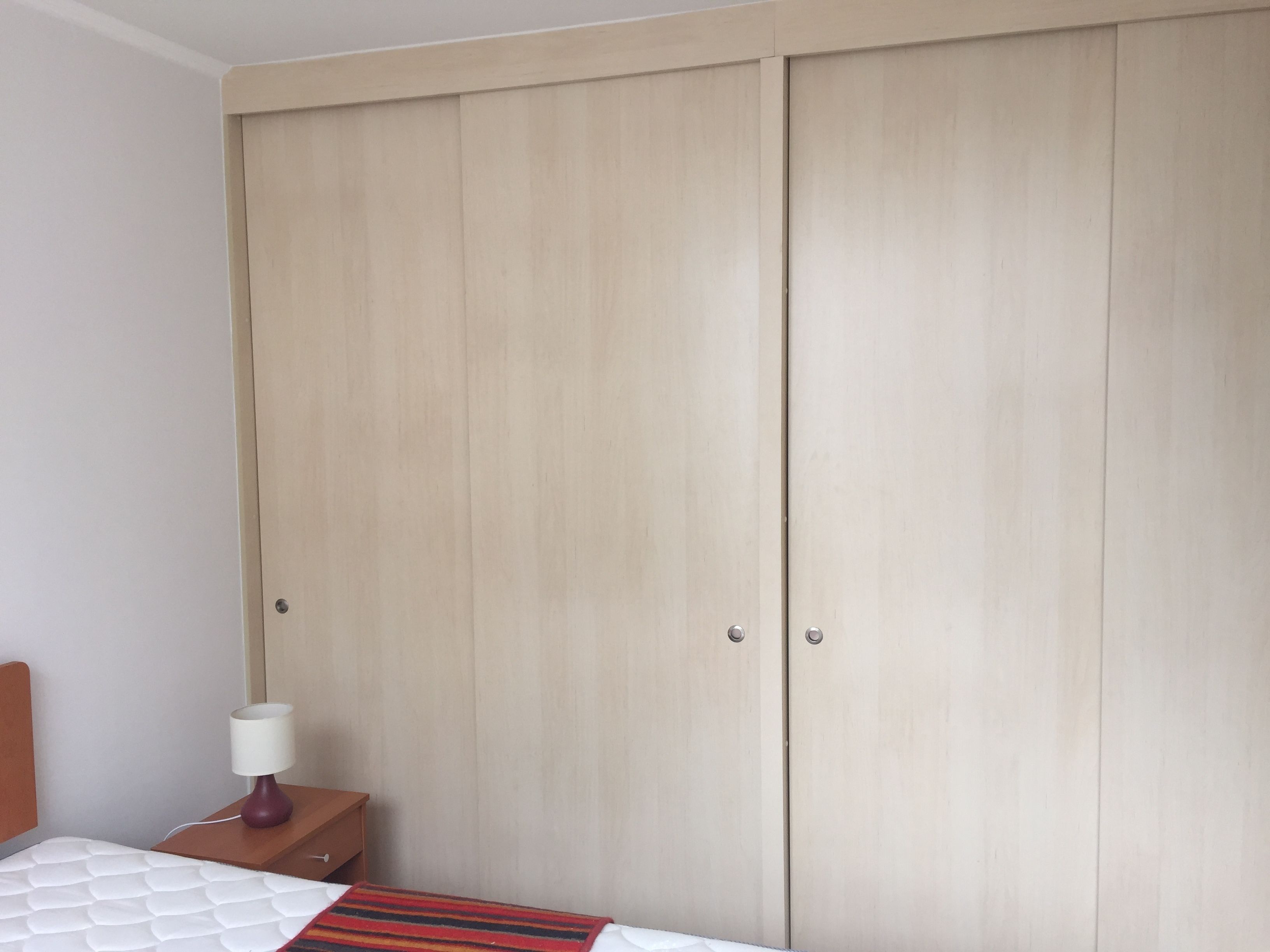 Un dormitorio con una cama, una mesita de noche, una lámpara y un armario.
