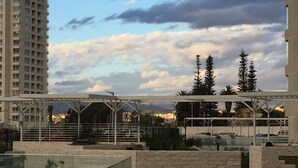 A rooftop terrace with a glass balustrade, a stone wall, and a view of a cityscape including a tall building and trees. - 13.- HNA Marina Sol 1 (Coquimbo)