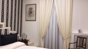 Ein Hotelzimmer mit einem Bett, einem Sessel, einem gerahmten Bild an der Wand und einem Fenster mit Vorhängen.