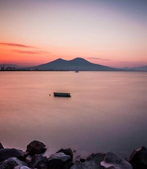 A calm body of water with a boat in the center, surrounded by rocks and a mountain in the background. - Royal Gismonda (Naples)