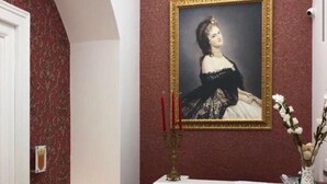Ein Empfangsbereich mit einer weißen Theke, einem gerahmten Porträt an der Wand und einem roten floralen Muster links an der Wand.
