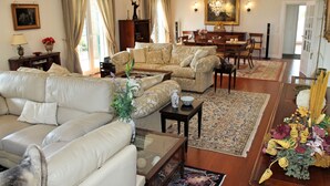 A spacious living room with a large sofa, a coffee table, and a dining area with a chandelier. - Villa Luzia by Our Madeira (Funchal)