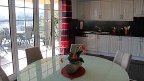 A modern kitchen with white cabinets, a glass dining table, and a view of the outdoors through large sliding doors. - Villa Luzia by Our Madeira (Funchal)