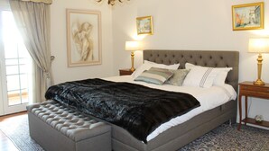A bedroom with a large bed, a chandelier, two bedside tables with lamps, and artwork on the walls. - Villa Luzia by Our Madeira (Funchal)