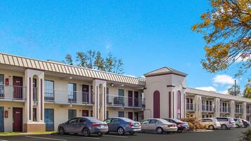 A motel with multiple-story buildings, each with balconies and a parking lot in front.