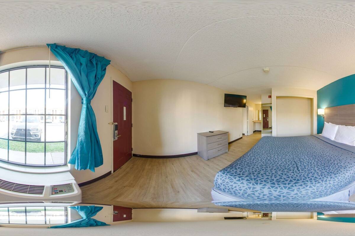 A modern hotel room with a large bed, a desk, and a window with curtains.