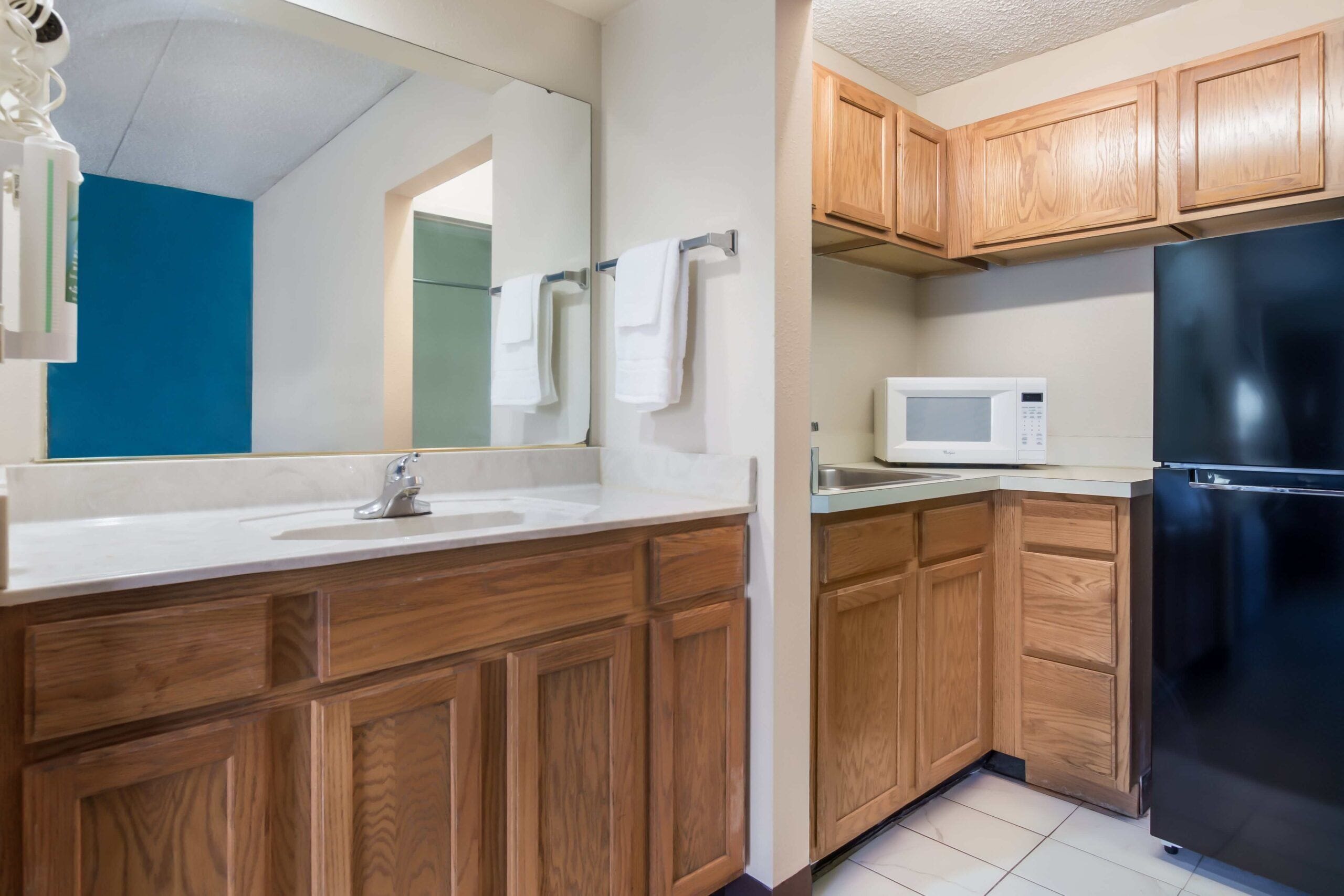 A modern kitchen with wooden cabinets, a stainless steel refrigerator, a microwave, and a sink.