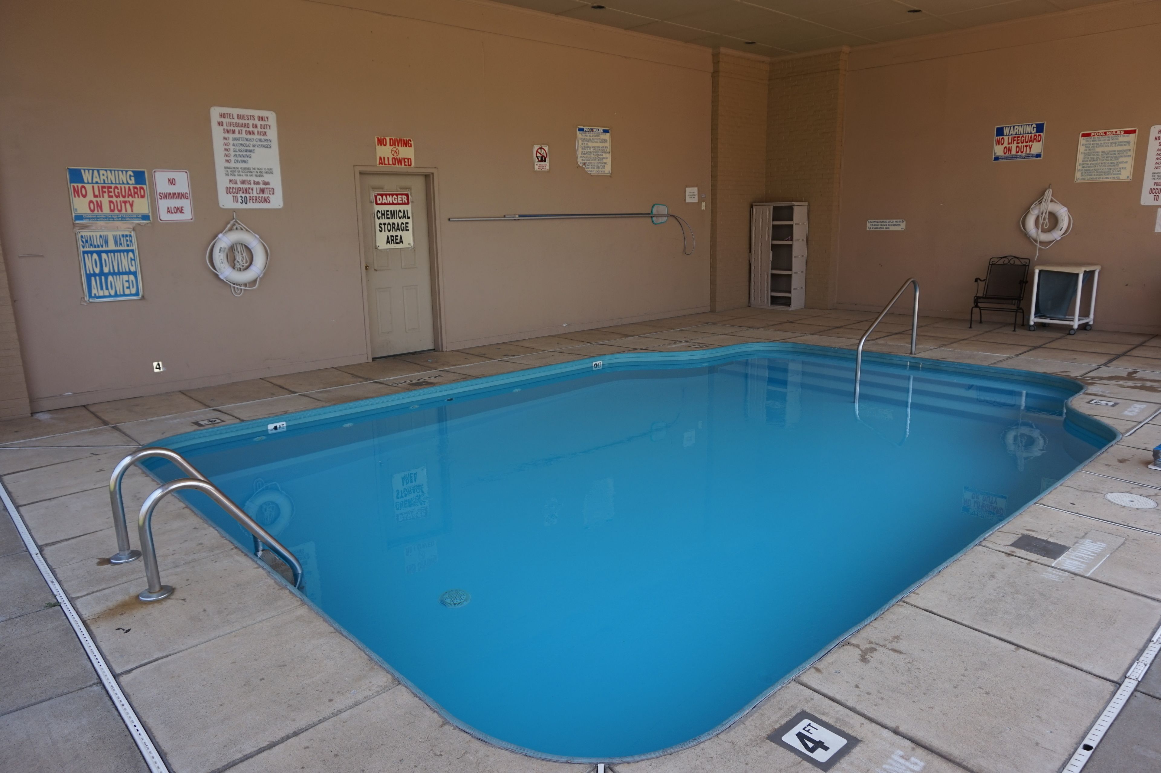 A swimming pool with safety signs, a diving board, and a lifebuoy.