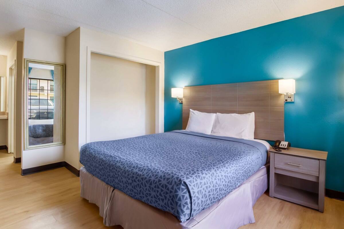 A hotel room with a bed, nightstand, and a view of the parking area.