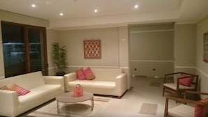Een ruime woonkamer met een witte zithoek, een salontafel en een houten stoel. Er is een groot raam met uitzicht op buiten.