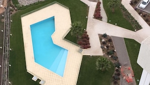 Luchtbeeld van een woonwijk met een zwembad, een omheinde tuin en een weg.