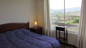 Un dormitorio con cama, mesita de noche, lámpara y ventana con vista a un paisaje.