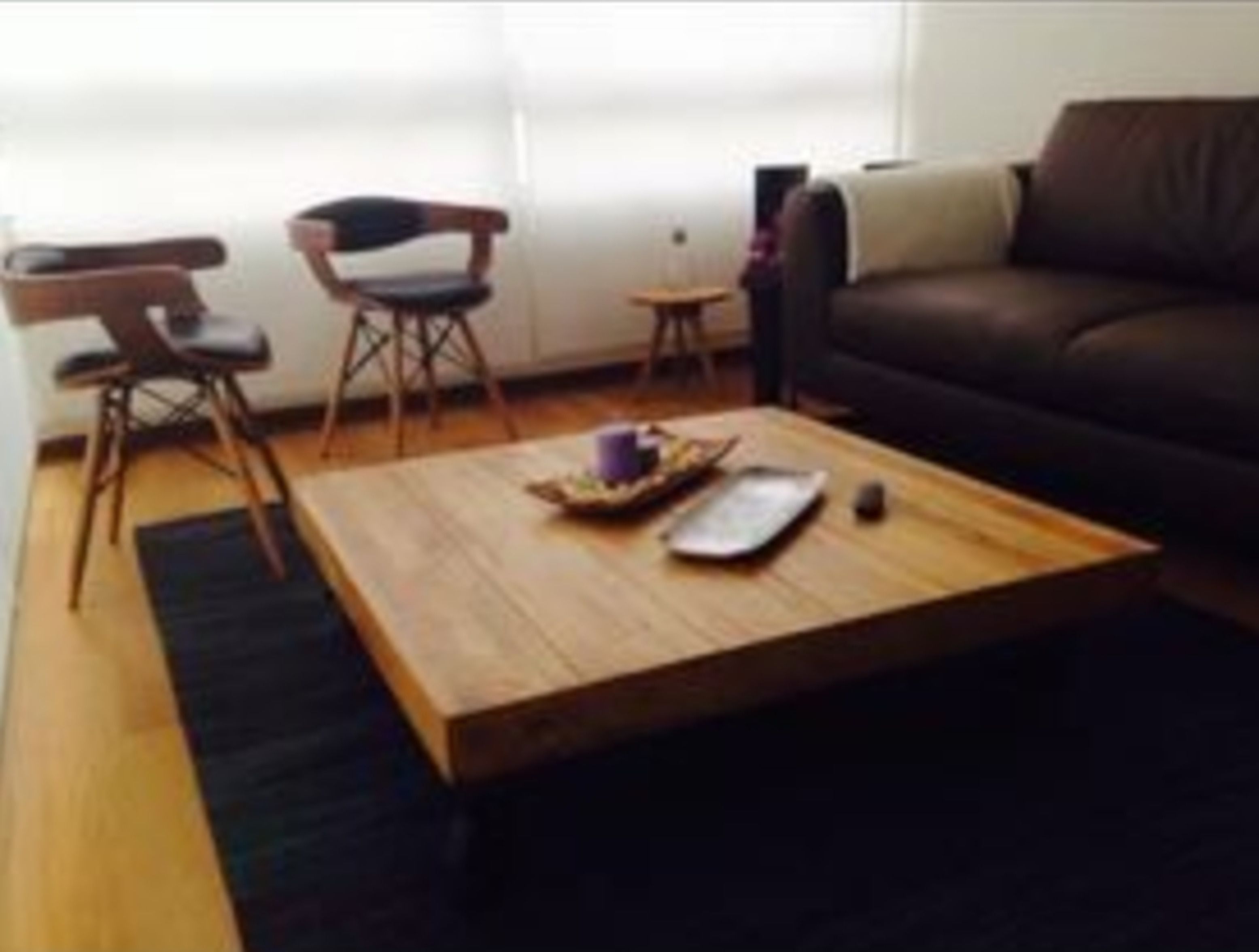 Una sala de estar con una mesa de centro de madera, dos sillas, un sofá y una mesita auxiliar.