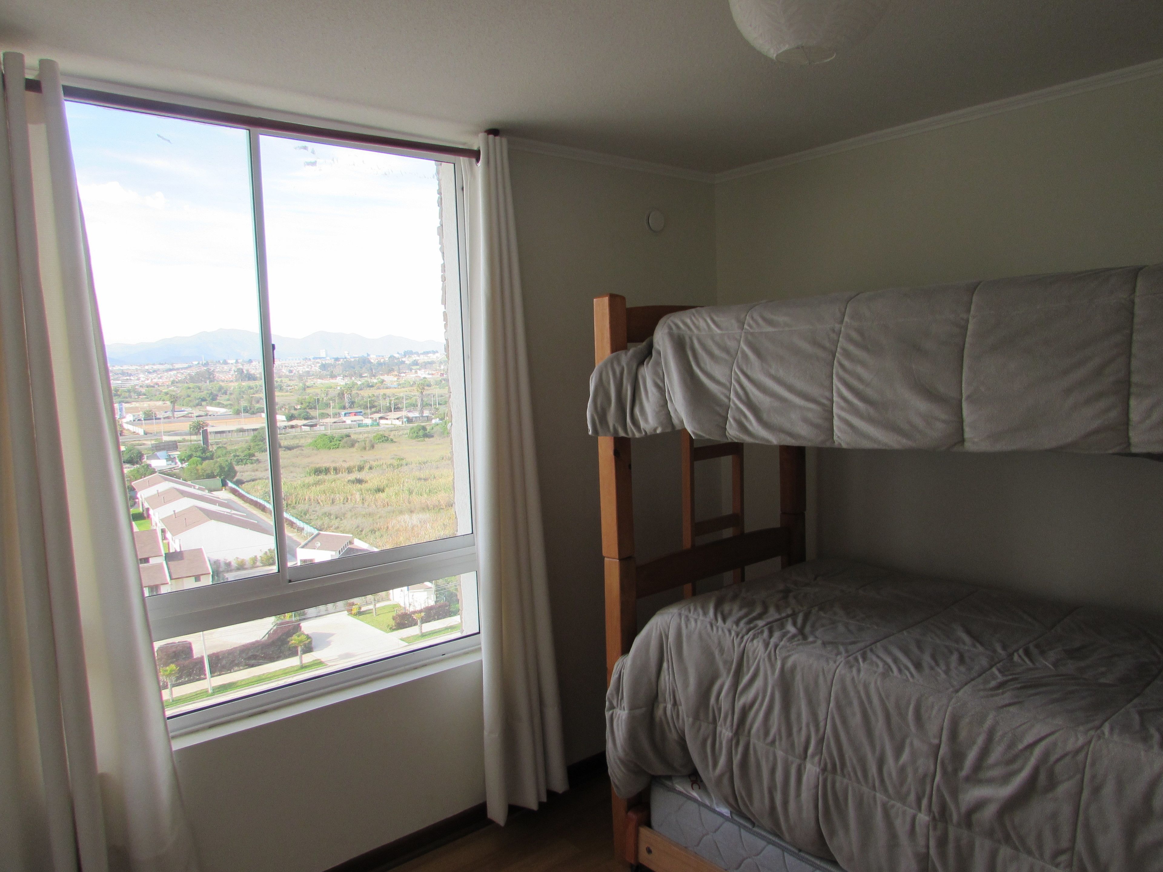 Une chambre avec des lits superposés et une fenêtre donnant sur un quartier résidentiel.