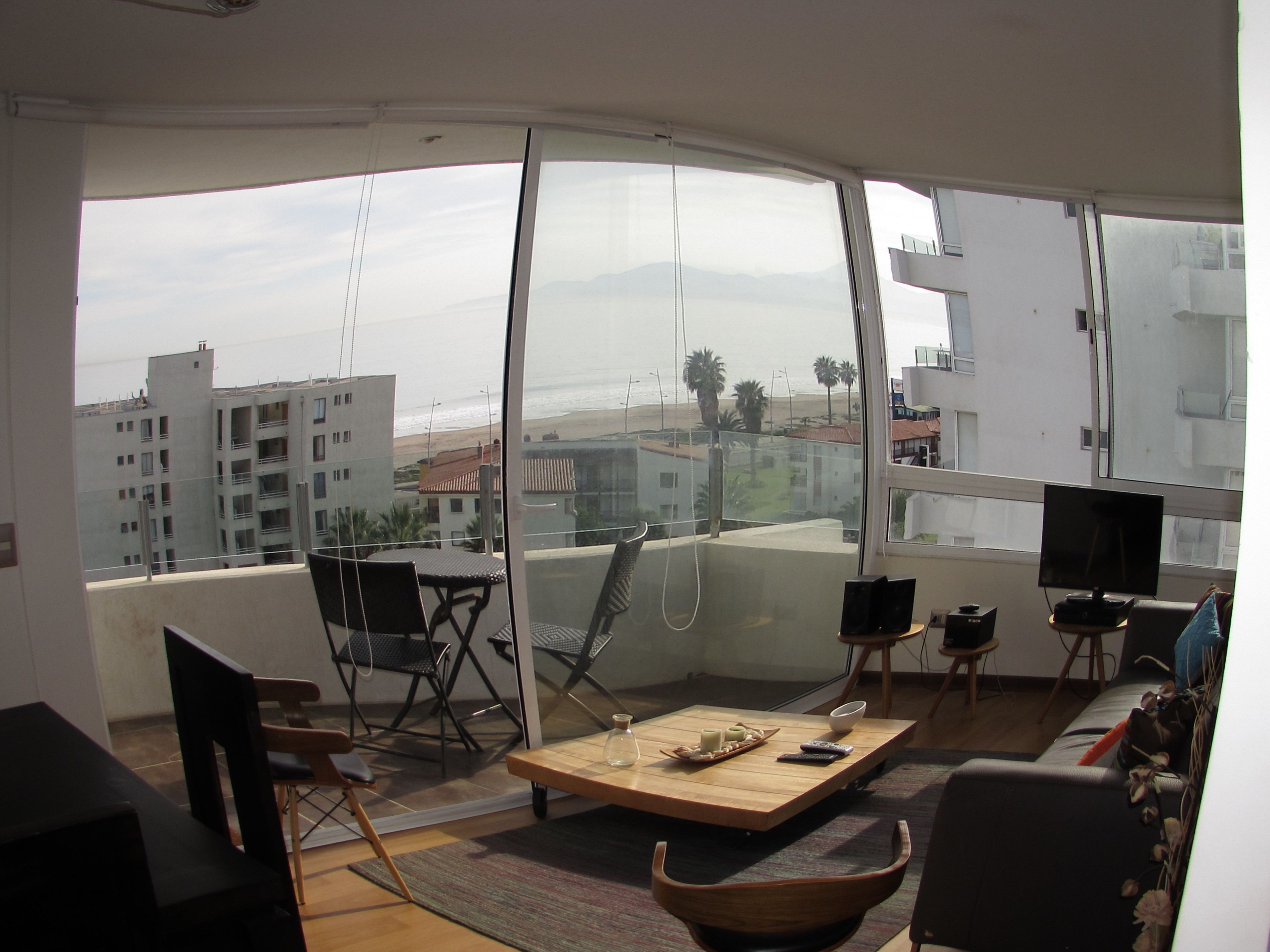 A modern living room with a large window, a wooden coffee table, a TV, and a sofa.
